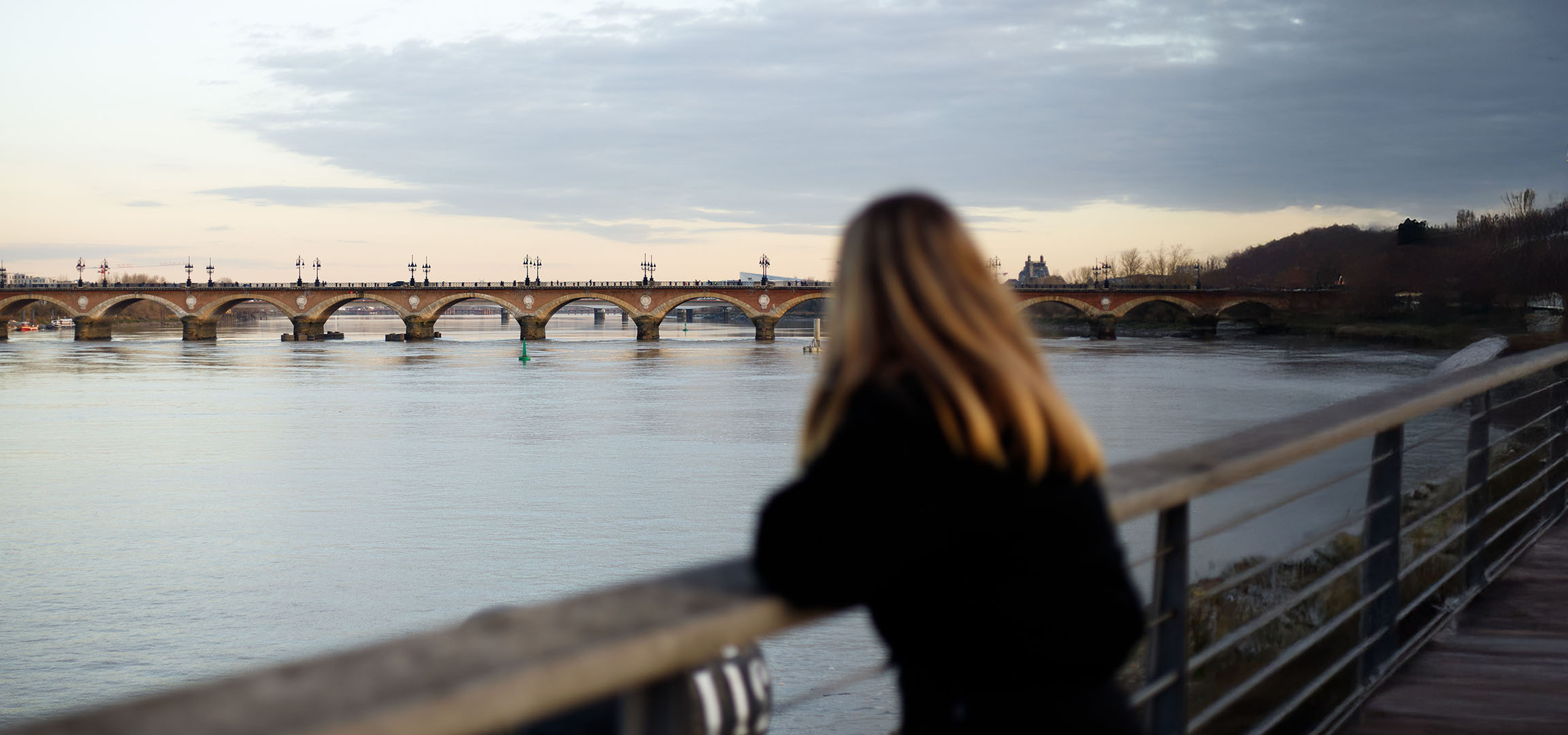 View of an arched bridge and a river, with a blurred person with long hair in the foreground.