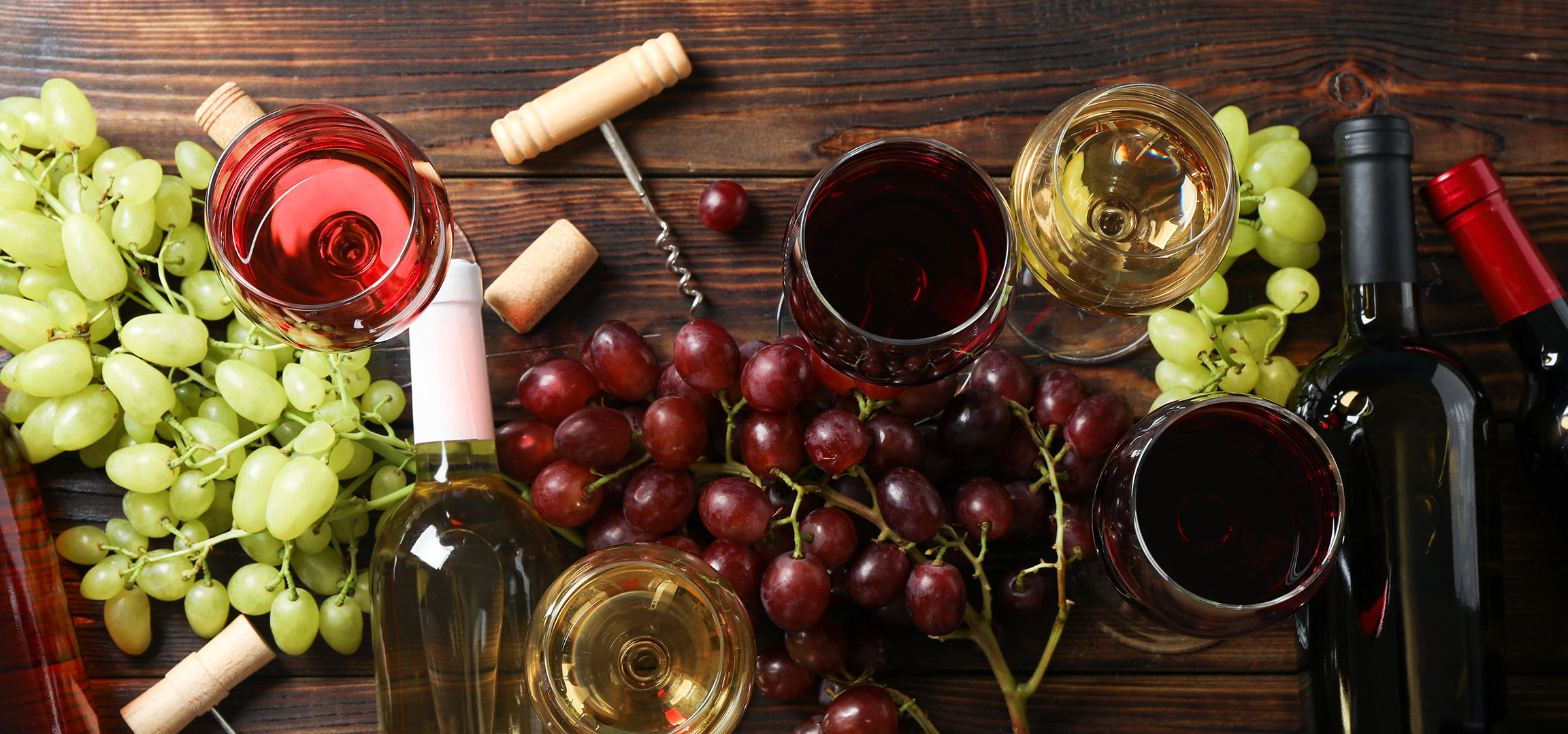 Various wines, grapes, and wine accessories on a wooden table.