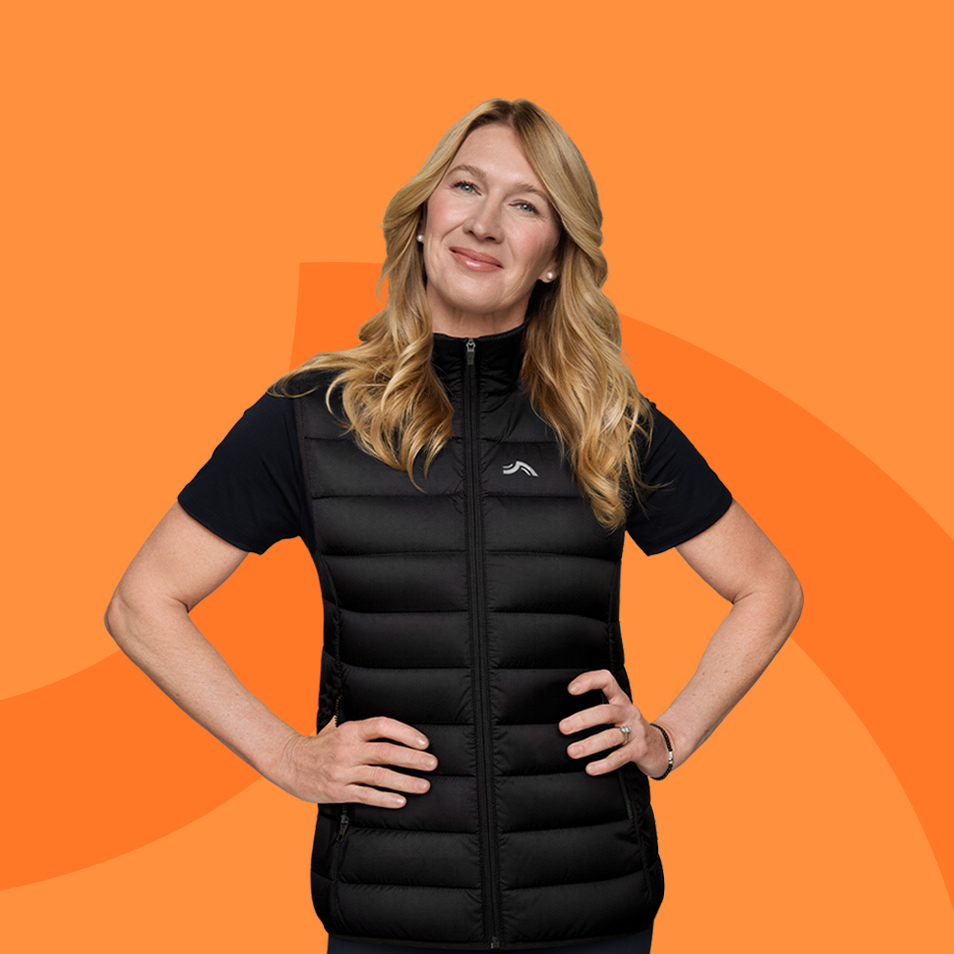 Woman in a black puffer vest and black t-shirt, smiling, against an orange background.