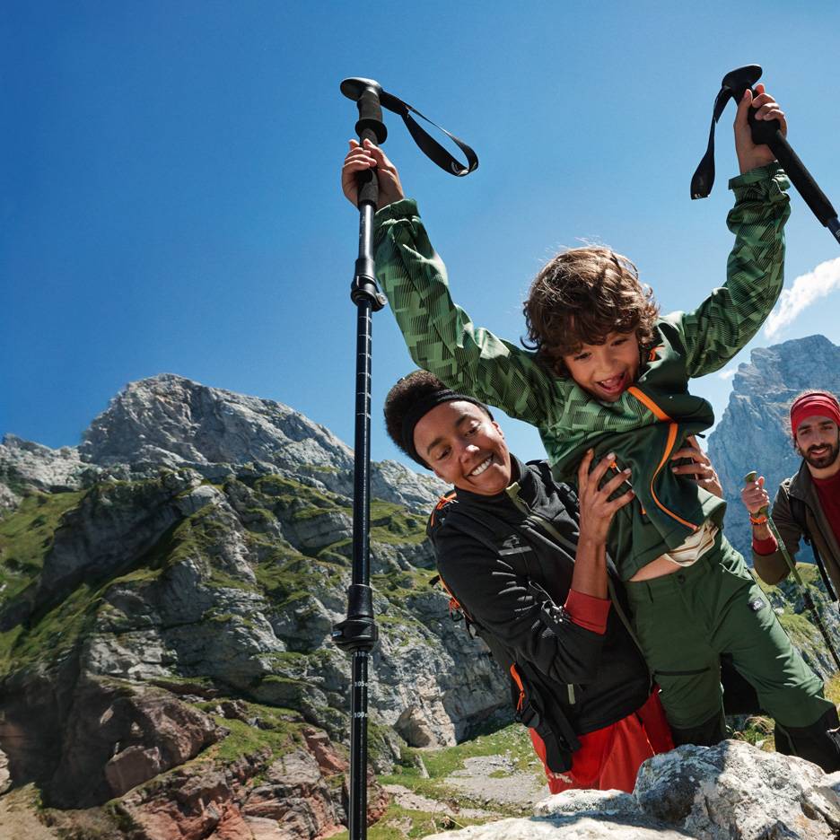 Family hiking with trekking poles and outdoor clothing in the mountains.
