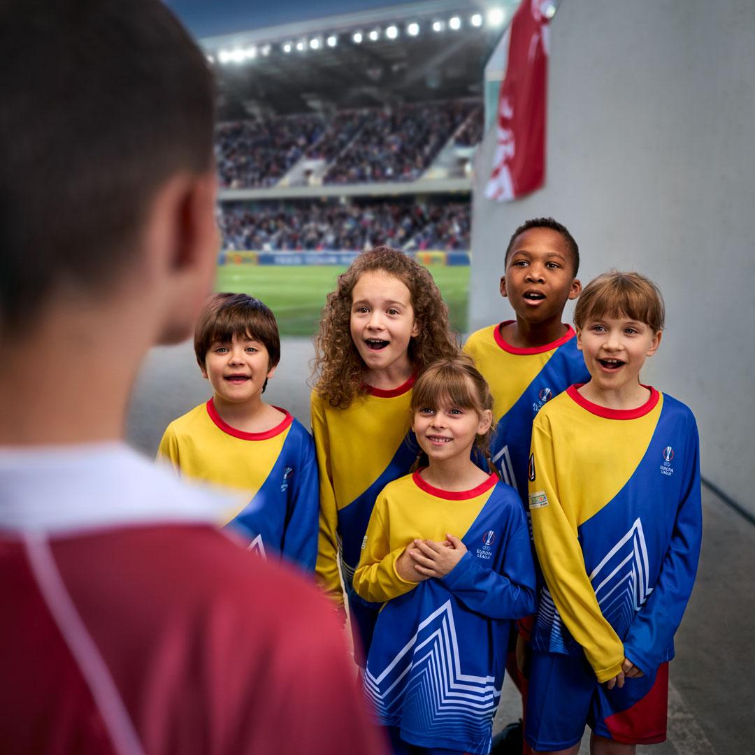 Children in yellow and blue football jerseys watching a player on the field.