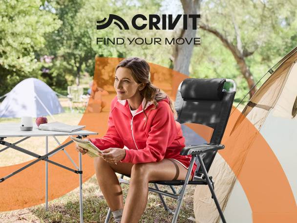 Woman in a red jacket sitting on a camping chair, reading, with a tent and table in the background.
