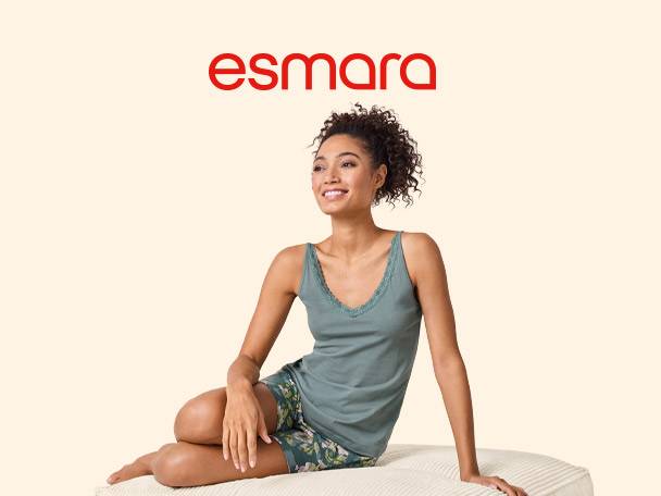 Woman in a green camisole and floral shorts, smiling and sitting on a cushion.