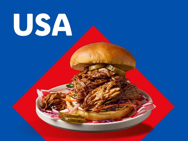 A pulled pork burger with pickles and coleslaw on a plate, with USA text on a blue background.