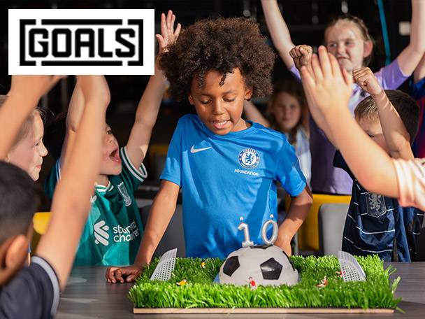 Kids celebrating a birthday with a football-themed cake, wearing Chelsea and Liverpool jerseys.