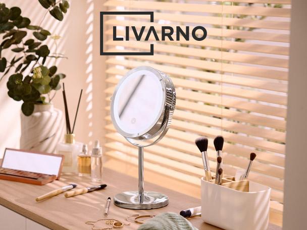 A vanity mirror with LED light, makeup brushes, and cosmetics on a wooden table.