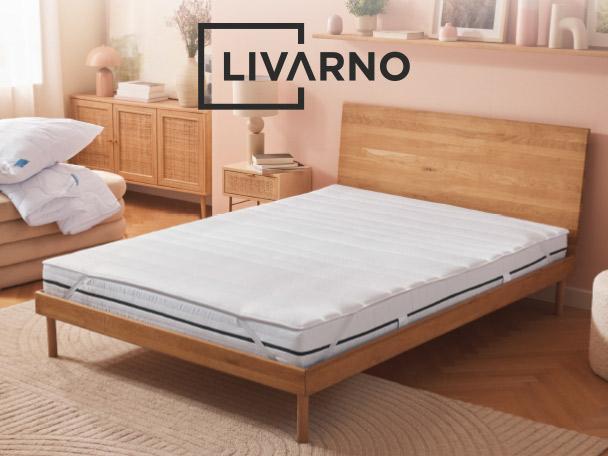 Bedroom with a wooden bed frame, white mattress, and stacked pillows and duvet.
