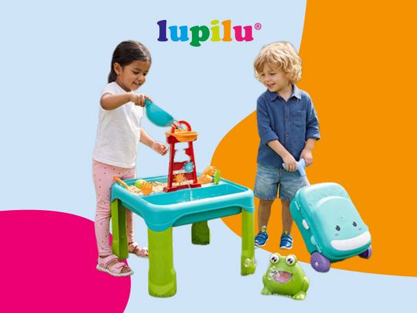 Two children playing with a sand and water table, a ride-on suitcase, and a frog toy.