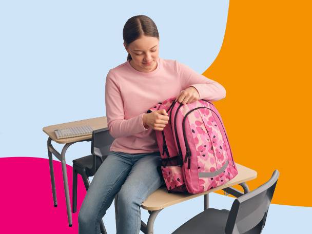 Girl in a classroom with a pink floral backpack, sitting on a desk.