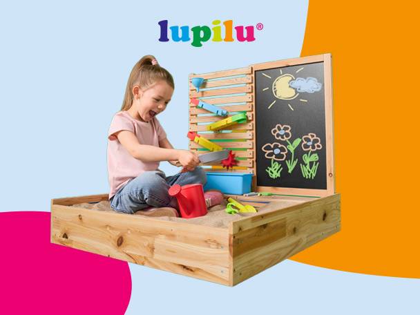 Happy girl playing in a wooden sandpit with a water wall and chalkboard.