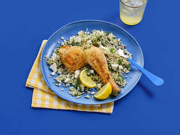 A roasted chicken leg with rice pilaf, feta, and lemon on a blue plate.