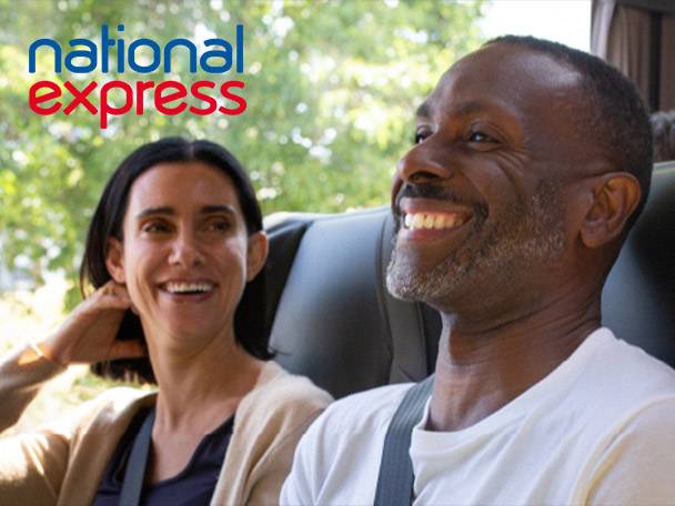 Two happy passengers on a National Express coach, smiling and looking out the window.