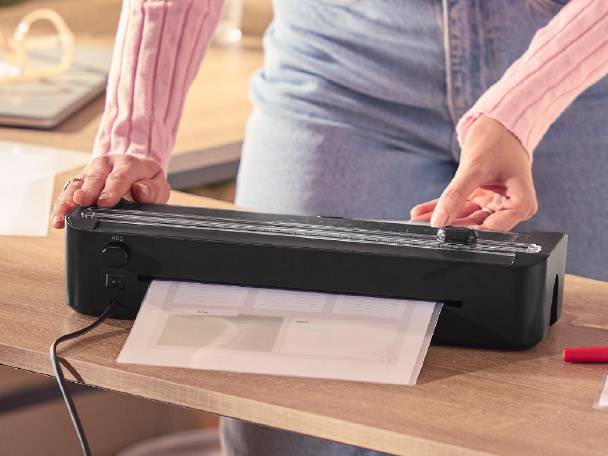Person laminating documents with a black laminator on a wooden desk.