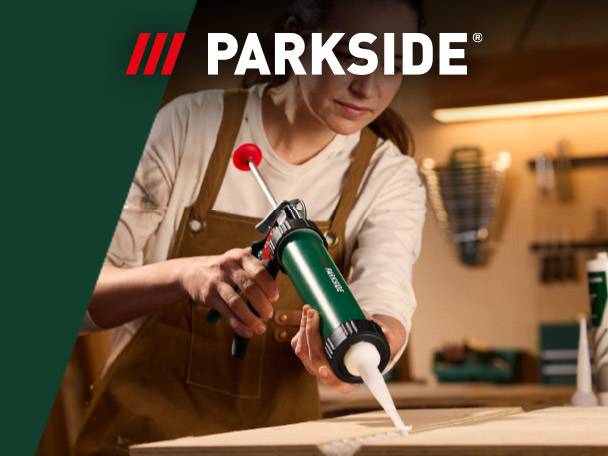 Woman in an apron using a green caulk gun to apply sealant to wood in a workshop.