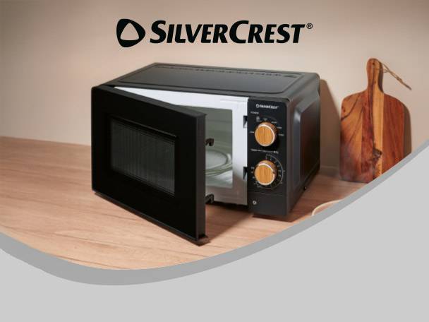 Black microwave oven with door open on a wooden counter next to a cutting board.