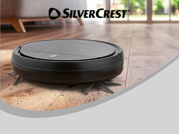 Robot vacuum cleaner on a wooden floor with dirt, with a living room in the background.