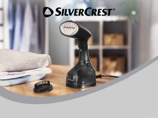 Handheld garment steamer with a brush attachment and folded clothes on a wooden table.
