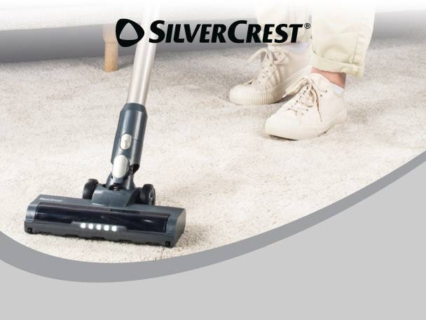 Cordless stick vacuum cleaner on a white carpet, with a person's feet in the background.