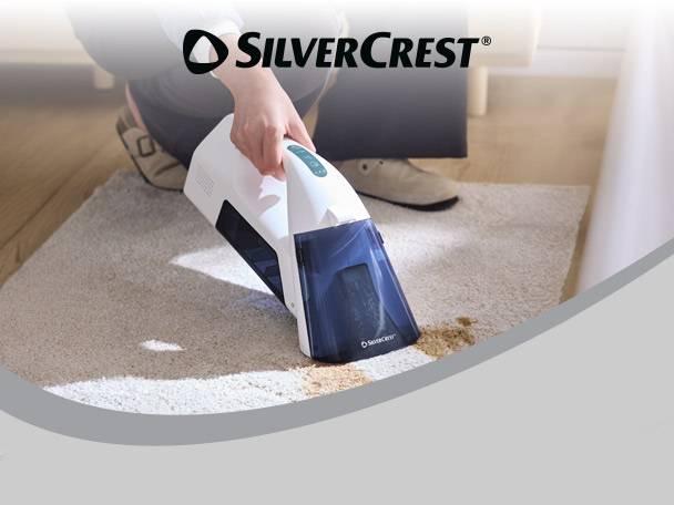 Person cleaning a spill on a rug with a handheld carpet cleaner.