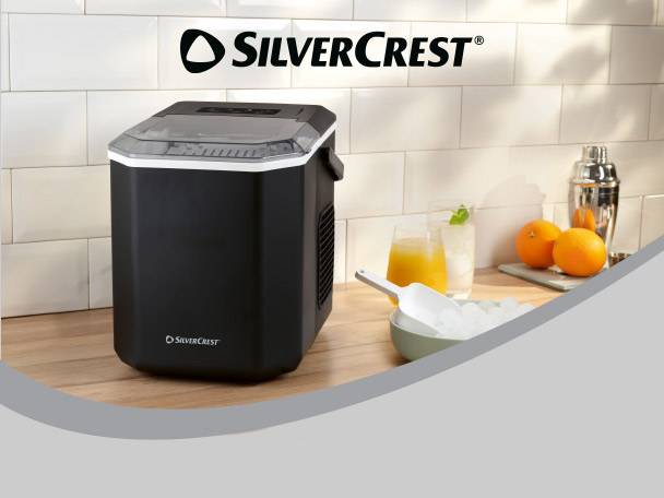 Black ice maker on a wooden counter with drinks, oranges, and a bowl of ice.
