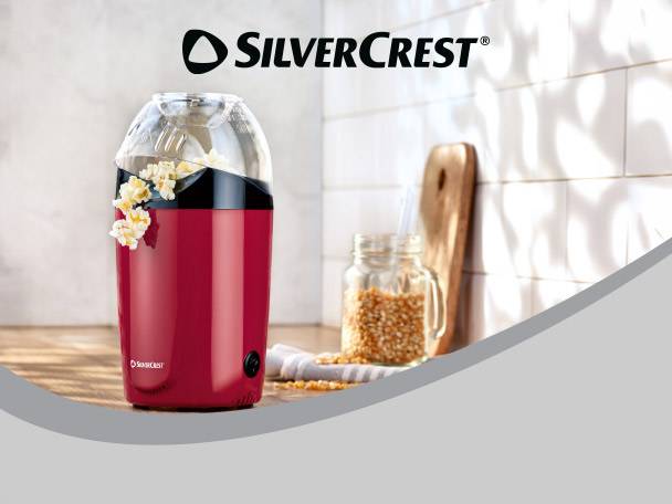 Red popcorn maker with popcorn spilling out, next to a jar of kernels.