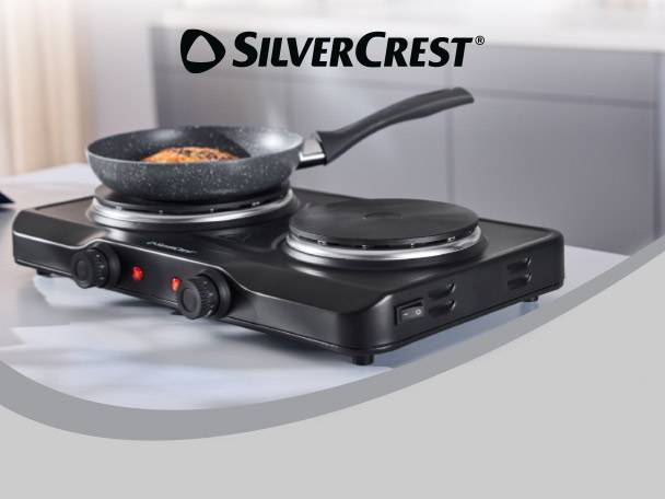 Black double hot plate with a frying pan on one burner, cooking food.