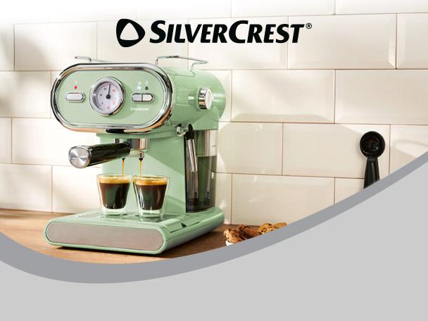 A retro-style espresso machine in mint green, brewing coffee into two small glasses on a wooden counter.
