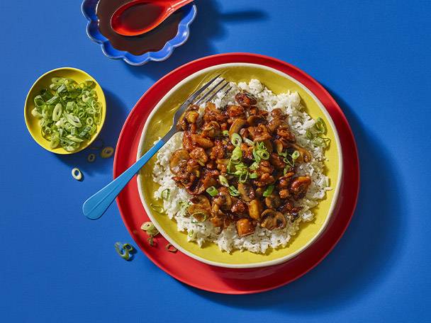 Teriyaki chicken and mushroom stir-fry with rice, garnished with spring onions.