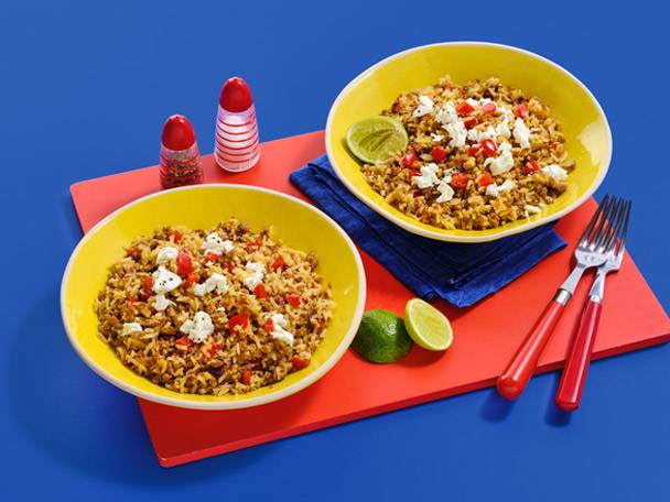 Two yellow bowls of rice with red peppers and white cheese, with salt and pepper shakers.