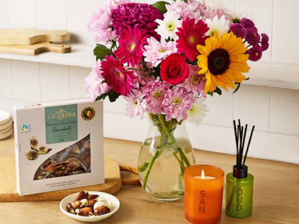 A vibrant bouquet of flowers, a box of Belgian chocolates, a candle, and a reed diffuser.