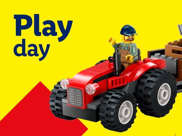 Lego minifigure on a red tractor with a trailer, text 'Play day' on yellow background.