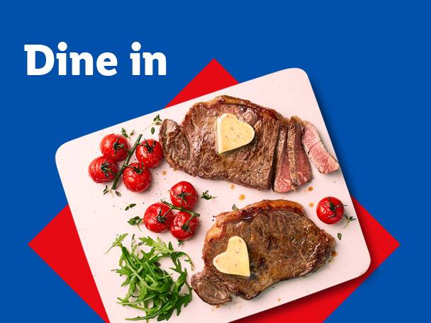 Two steaks with heart-shaped butter, cherry tomatoes, and rocket on a white board. Text: Dine in.