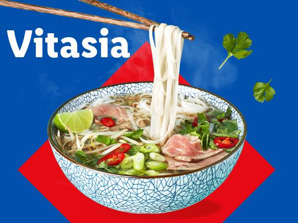 Pho noodle soup with beef, lime, and herbs, with chopsticks lifting noodles.