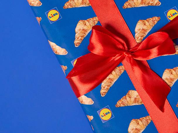 Lidl-branded gift wrap with croissants and a red ribbon bow on a blue background.
