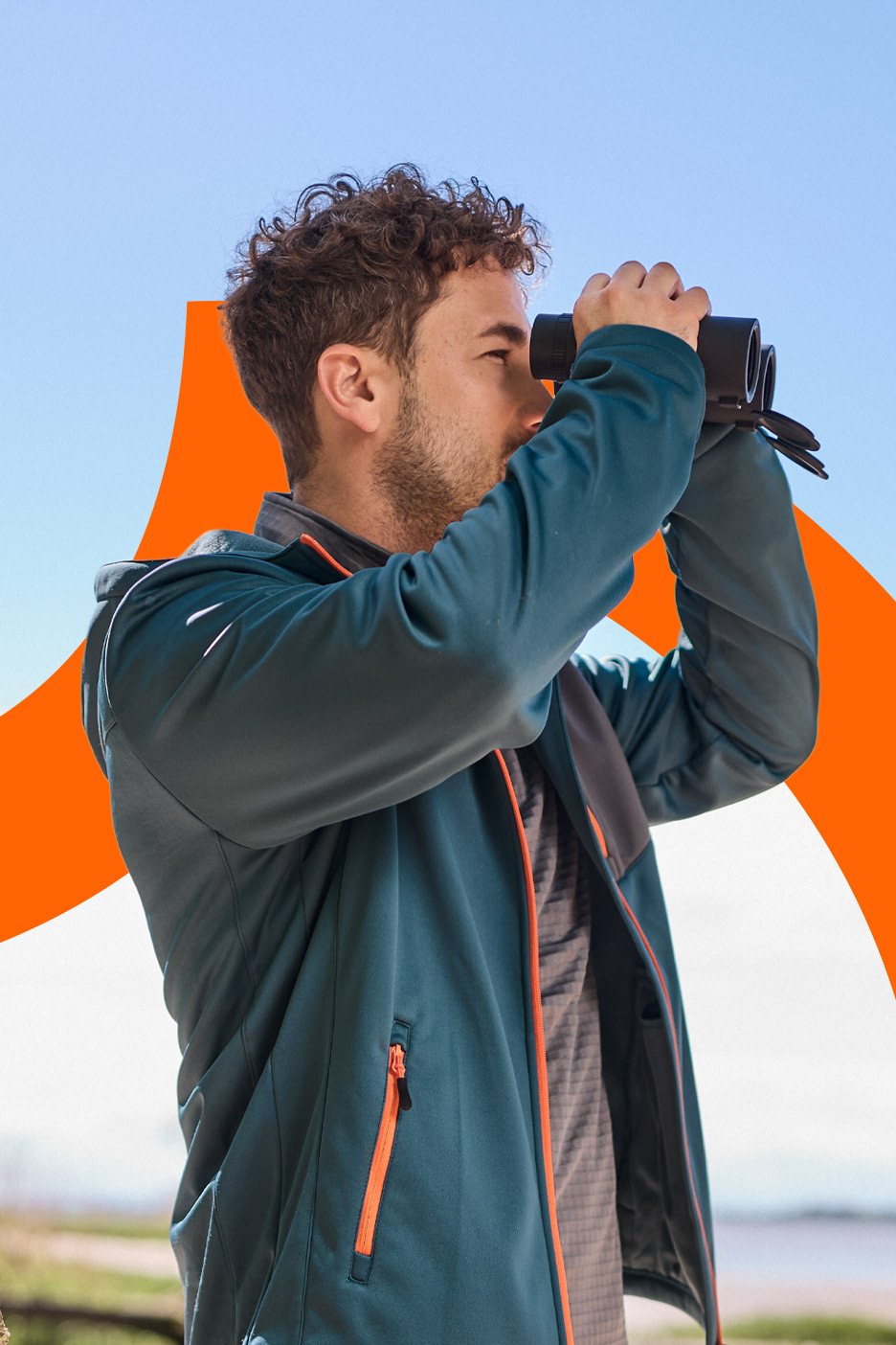 Man in a teal jacket with orange accents, looking through binoculars outdoors.