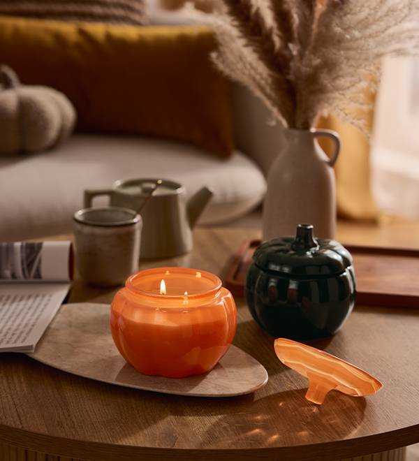 Pumpkin-shaped candles and decor on a coffee table, with a cozy living room in the background.