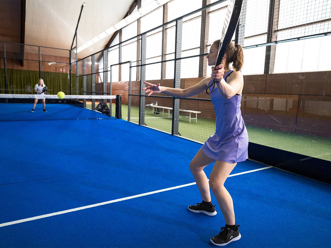 Woman in purple dress playing padel on a blue court.