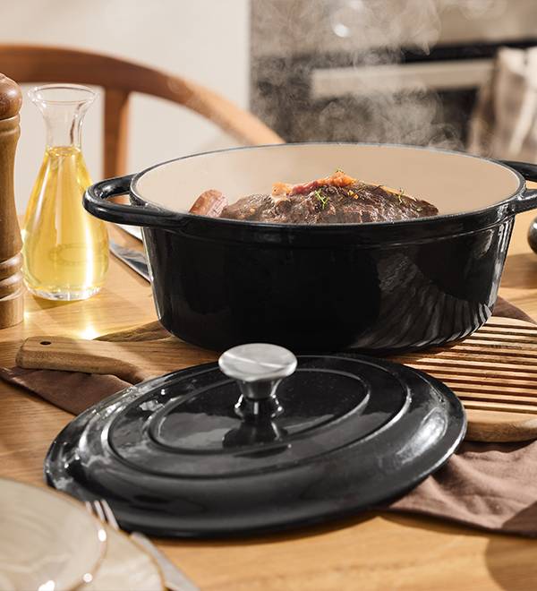 A black enameled cast iron Dutch oven with a lid, filled with braised meat, on a wooden table.
