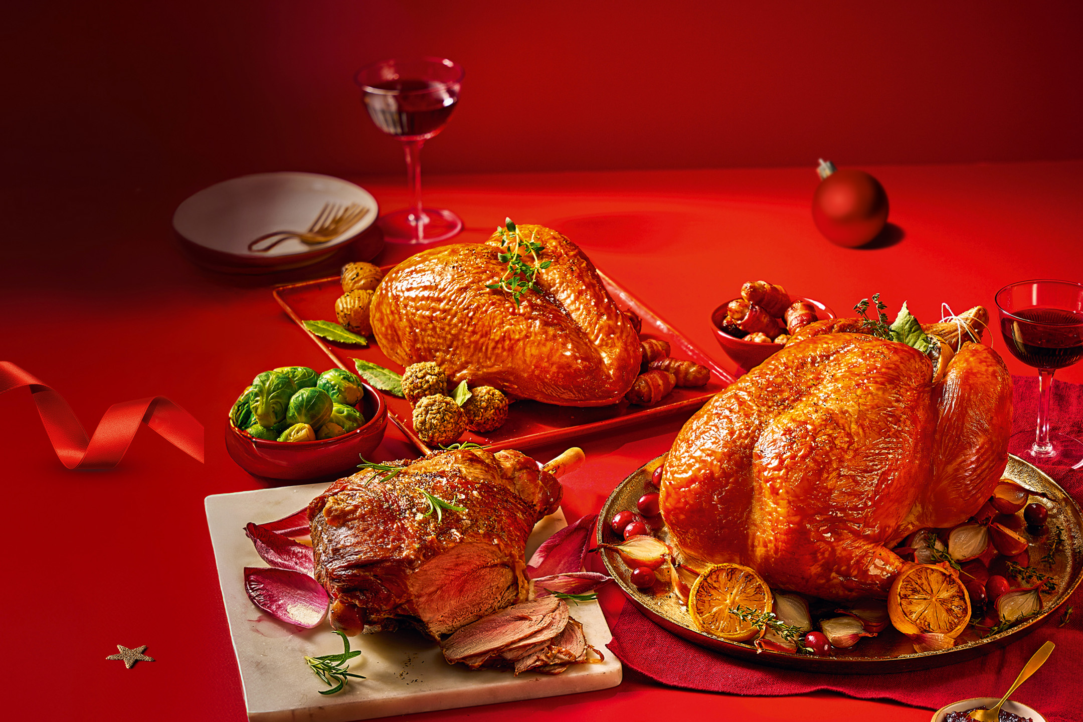 Christmas feast with roasted turkey, lamb, and sides on a red table.