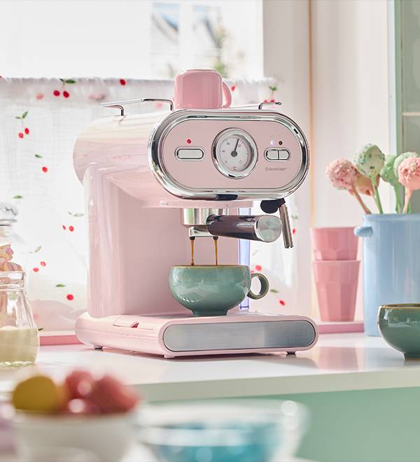 A pink retro-style espresso machine brewing coffee into a teal cup on a kitchen counter.