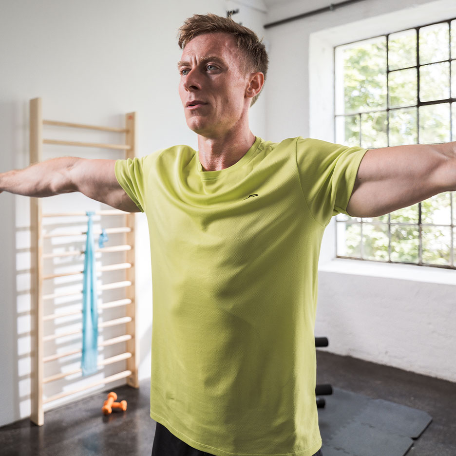Man in green athletic t-shirt exercising in a gym.