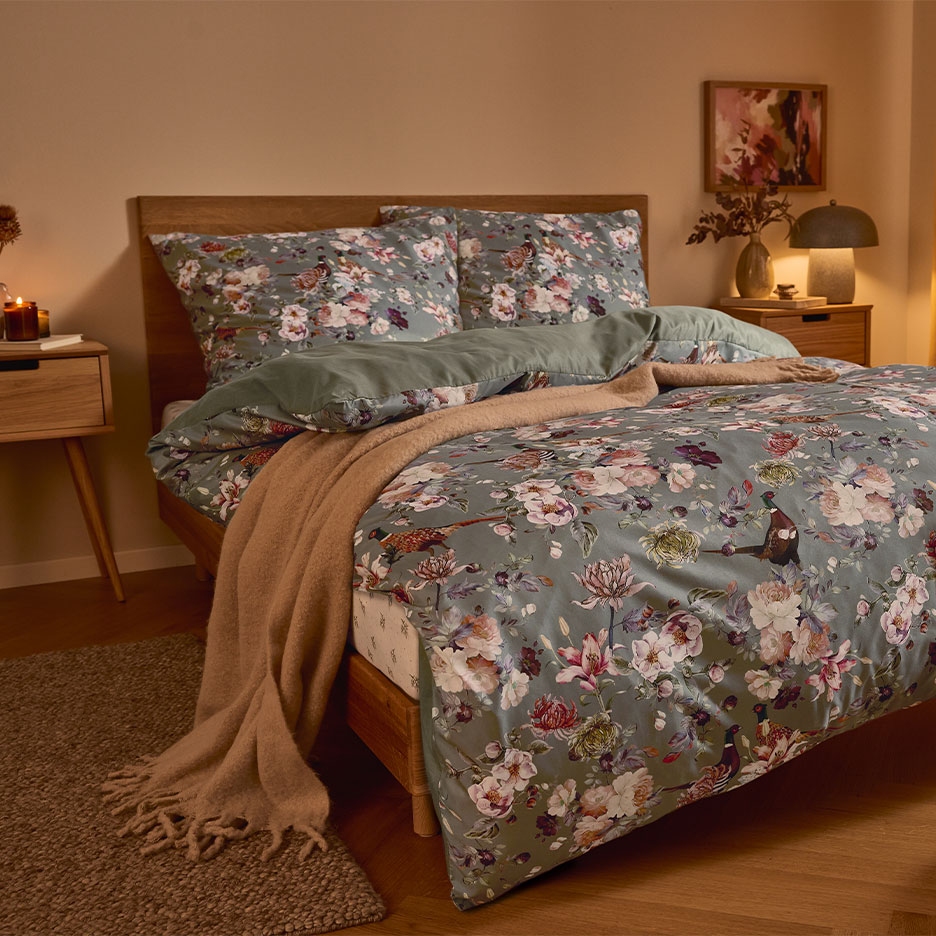 Wooden bed with green floral bedding and a brown throw blanket.