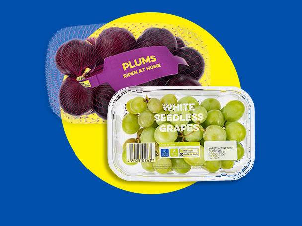 Plums in a net bag with a 'Ripen at Home' label and a clear plastic container of white seedless grapes.