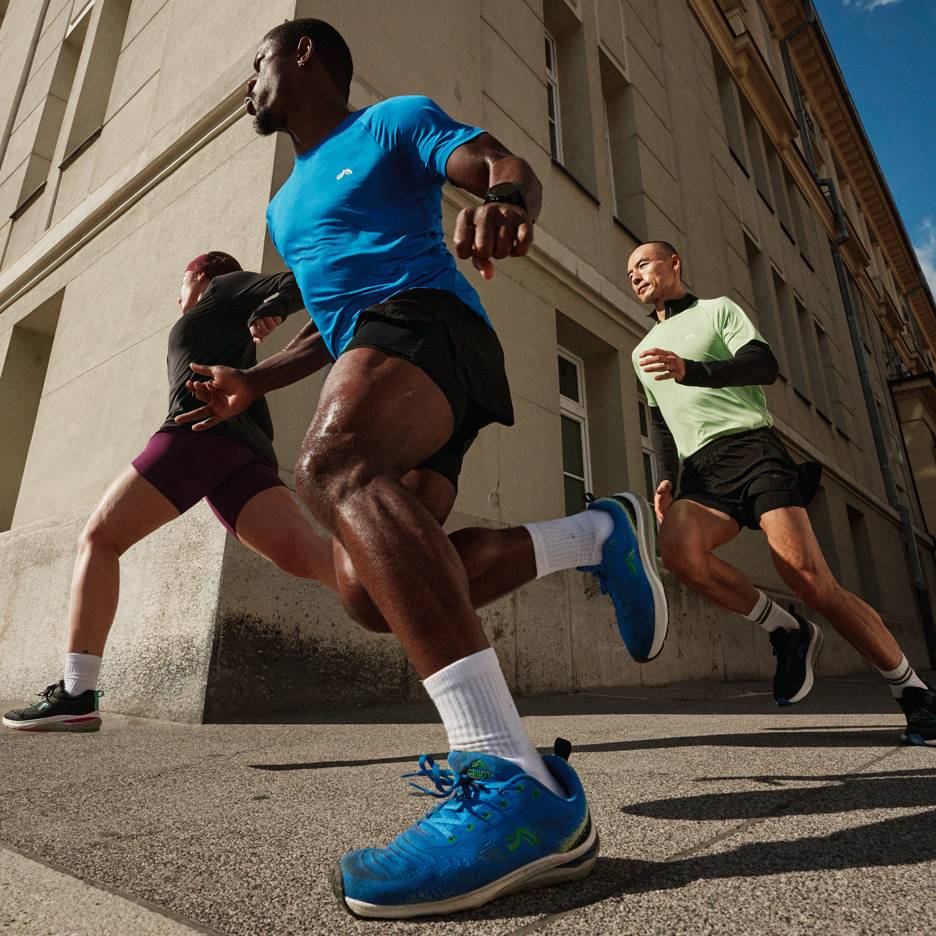 Three runners in sports shirts and shorts run down a city street.