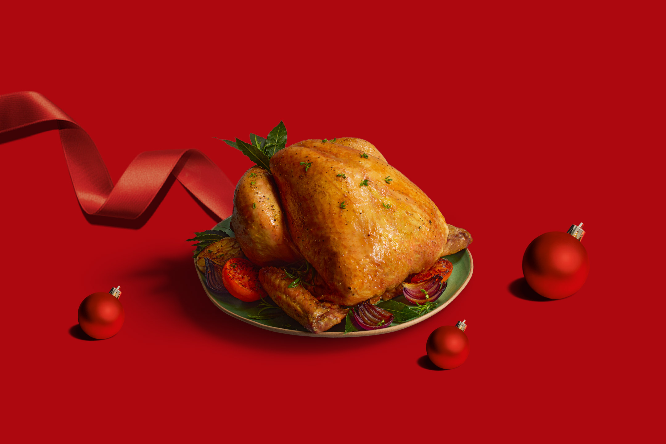 Roasted chicken with vegetables on a plate, red ribbon, and Christmas ornaments.