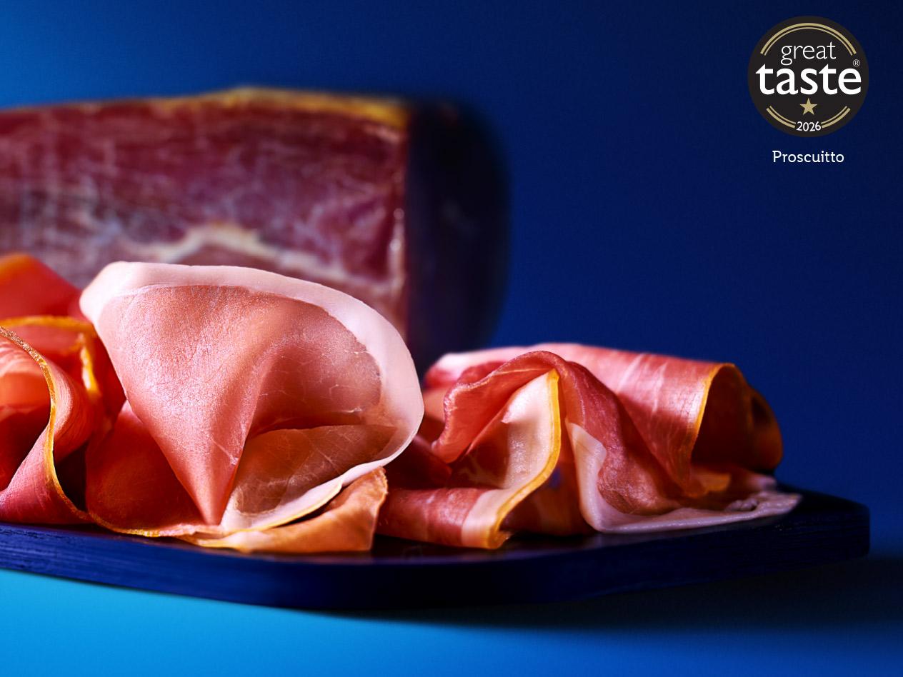 Slices of prosciutto on a dark board with a block of cured ham in the background.