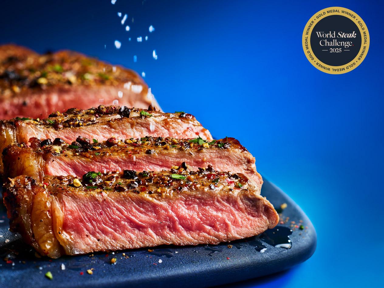 Slices of seasoned, medium-rare steak on a blue board with a gold medal award logo.
