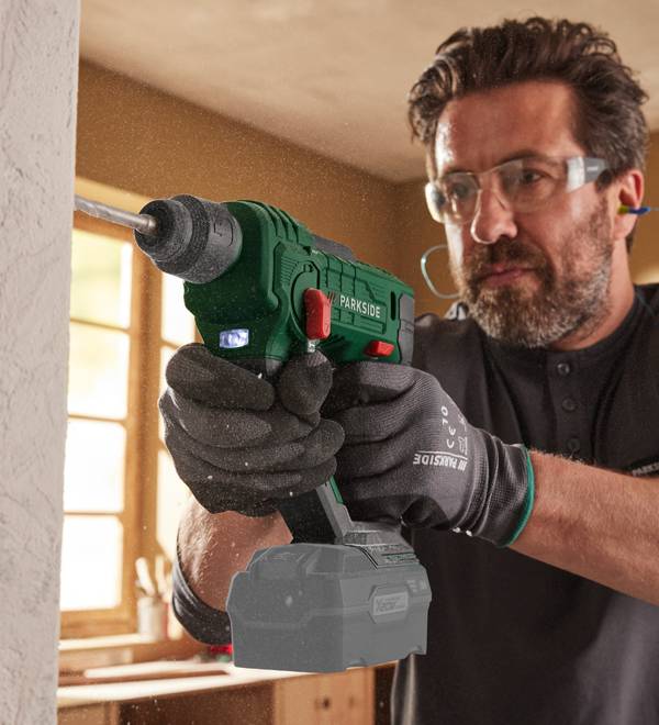 A man in safety glasses and gloves uses a Parkside drill to make a hole in a wall.