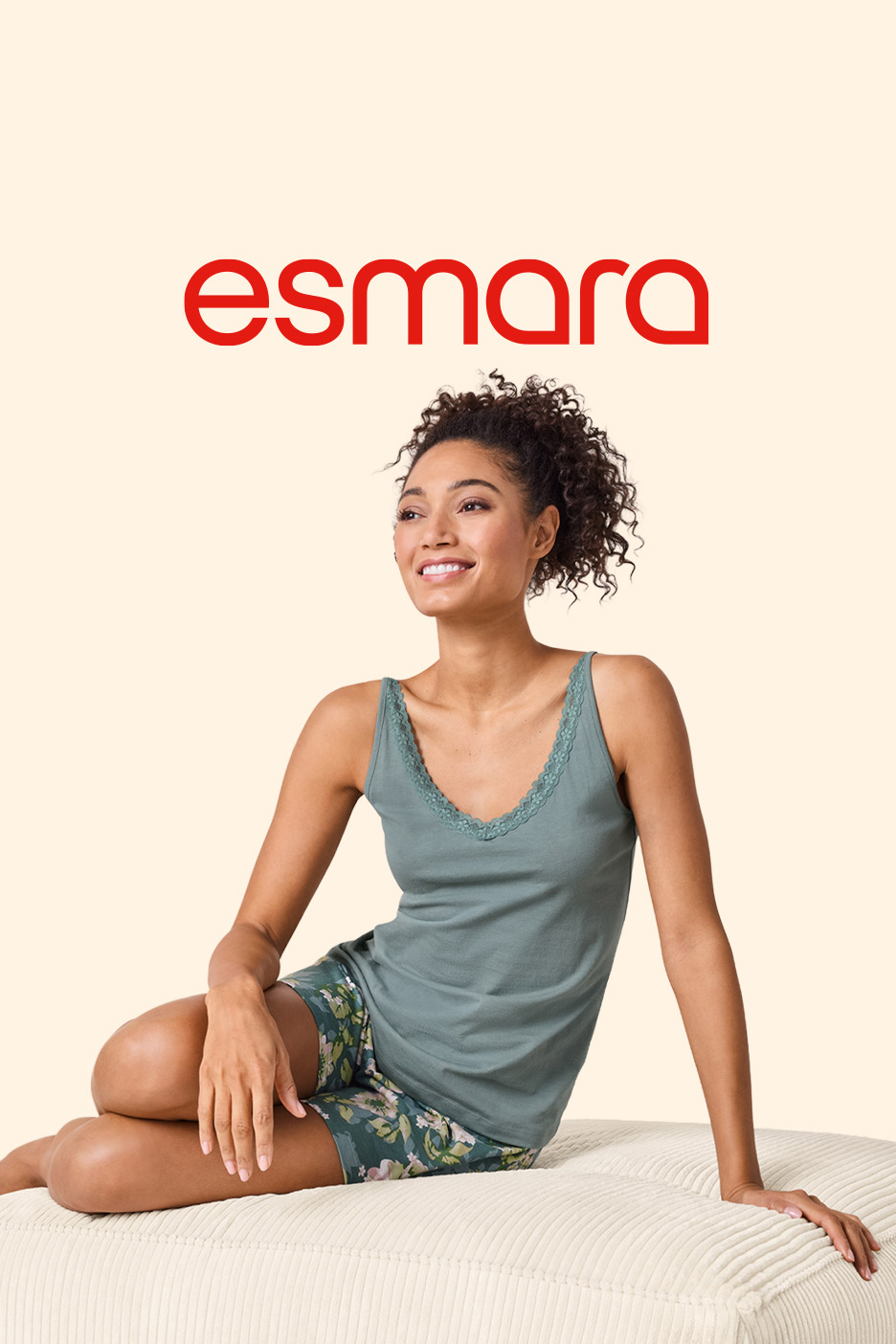 Woman in green lace-trim camisole and floral shorts, smiling and sitting on a cushion.
