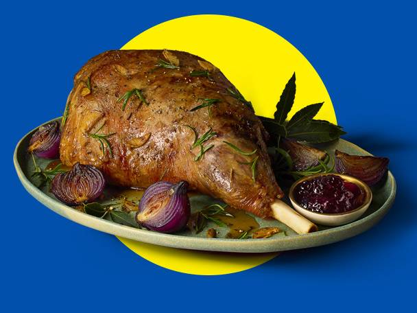 Roasted lamb leg with rosemary, garlic, red onions, and cranberry sauce on a plate.